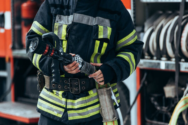 обрезанный выстрел пожарного в защитной форме с водяным шлангом в руках

