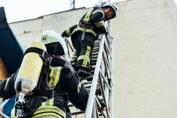 selective focus of firefighters in fireproof uniform standing on ladder