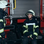 Bomberos con uniforme ignífugo y cascos conversando en la estación de bomberos