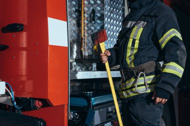partial view of firefighter in fireproof uniform holding axe at fire department clipart