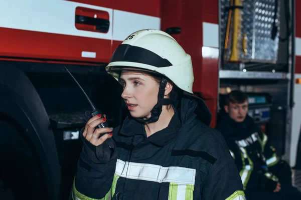 female firefighter talking on portable radio set with colleague behind at fire station