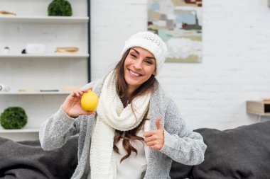 limon tutarak ve başparmak gösterilen sıcak giysiler içinde gülümseyen genç kadın