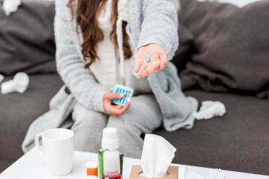 cropped shot of sick woman in warm clothes holding pill in hand clipart