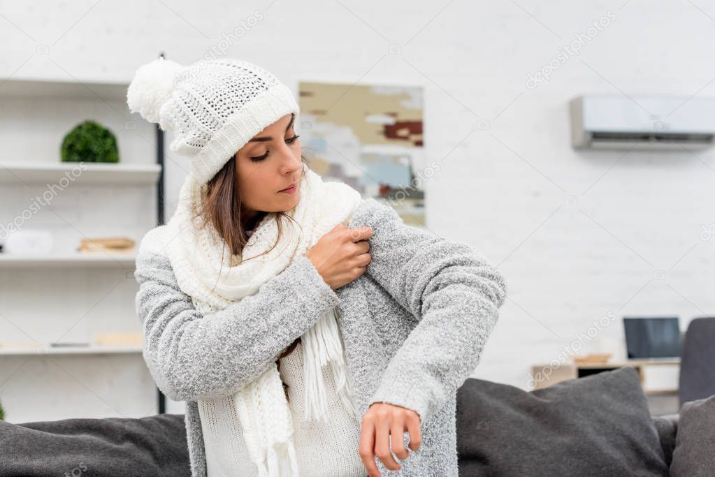 freezed young woman putting on warm clothes with air condition hanging on background