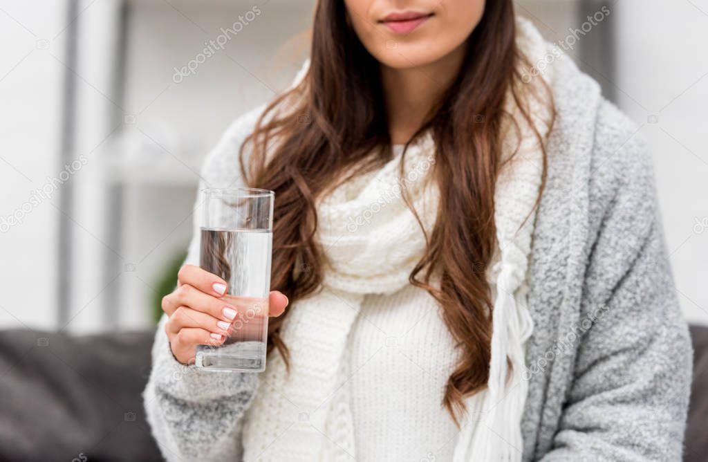 cropped shot of young woman in warm clothes holding glass of water