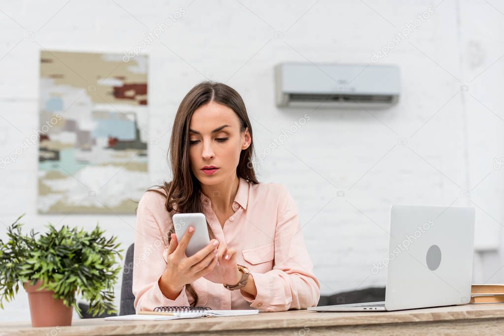 attractive young businesswoman using smartphone while working at office