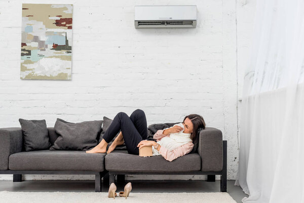 side view of sick young woman lying on couch at home