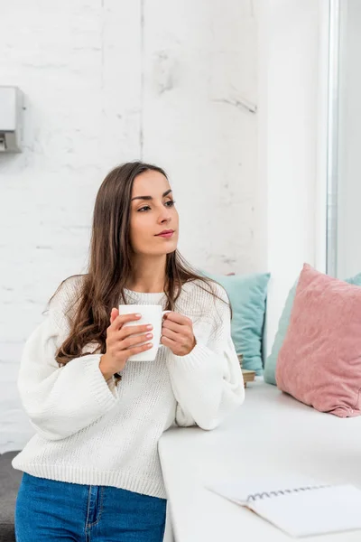 Atractiva Mujer Joven Sosteniendo Taza Café Mientras Apoya Alféizar Ventana — Foto de Stock