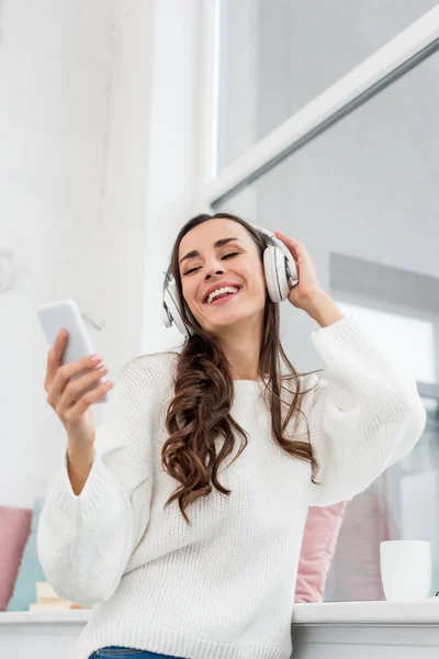 Vista Inferior Joven Sonriente Escuchando Música Con Teléfono Inteligente Auriculares —  Fotos de Stock