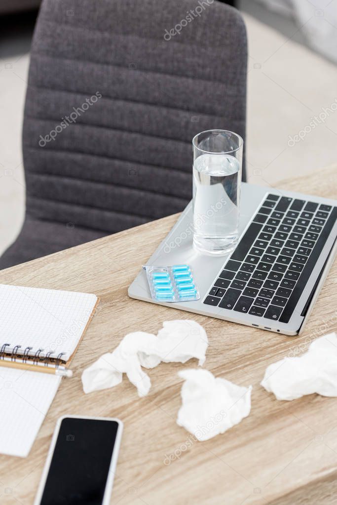 close-up shot of office workplace with laptop, glass of water and blister of pills