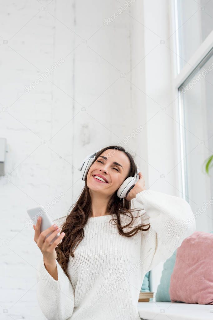 smiling young woman listening music with smartphone and wireless headphones at home