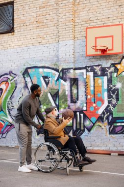 adam tekerlekli sandalyede ve mutlu Afro-Amerikan erkek basketbol birlikte sokakta oynayan kıdemli devre dışı