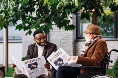 mutlu kıdemli adam tekerlekli sandalye ve Afrikalı-Amerikalı adam birlikte sokakta Gazeteler okuma devre dışı