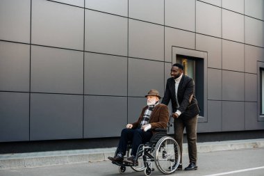 Kıdemli tekerlekli sandalye ve genç Afro-Amerikan cuidador street tarafından sürme erkekte devre dışı