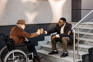 Kıdemli birlikte kahve içme ve kağıt bardak sokakta tungur tekerlekli sandalye ve Afrikalı-Amerikalı adam erkekte devre dışı