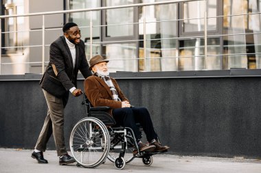 mutlu kıdemli tekerlekli sandalye ve Afro-Amerikan cuidador street tarafından sürme erkekte devre dışı