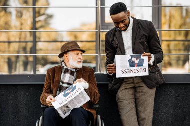 adam tekerlekli sandalyede ve Gazeteler birlikte sokakta okuma mutlu Afro-Amerikan erkek kıdemli devre dışı