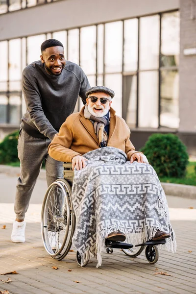 格子縞で車椅子の人とアフリカ系アメリカ人街に乗って幸せな先輩が無効に — ストック写真