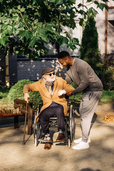 African American Man Pomaga Senior Niepełnosprawny Człowiek Wstać Wózka Inwalidzkiego — Zdjęcie stockowe