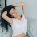 High angle view of curly attractive girl with closed eyes in bedroom at home