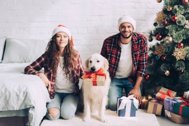 mutlu genç çiftle Noel Baba şapkaları ve altın geri almak ağız Noel'de evde hediye kutusunda