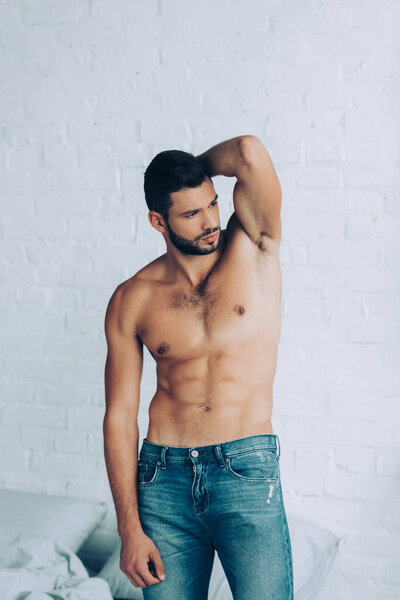 красивый мужчина без рубашки с мускулистым туловищем позирует в спальне дома
