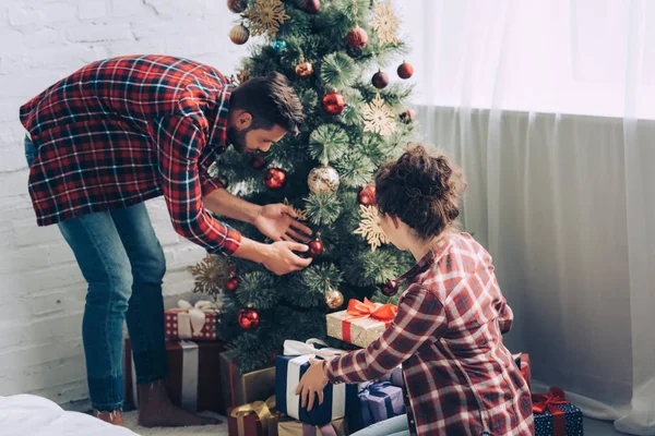 自宅のクリスマス ツリーを飾る市松模様のシャツでカップル — ストック写真