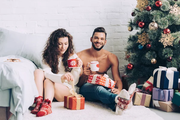 Feliz Jovem Casal Com Xícaras Café Sentado Perto Caixas Presente — Fotografia de Stock