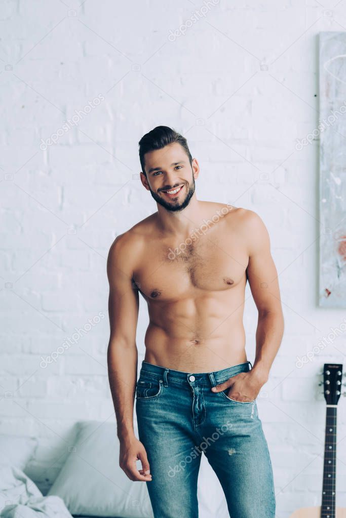 smiling shirtless man with muscular torso posing in bedroom at home