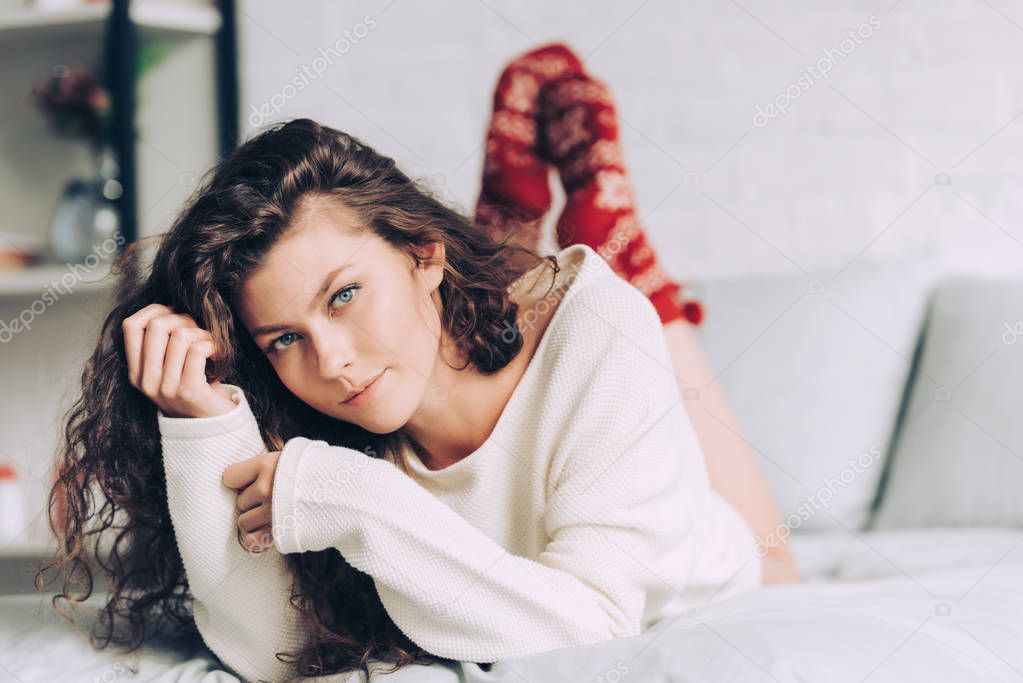 pretty young girl in white sweater and red socks looking at camera in bedroom at home