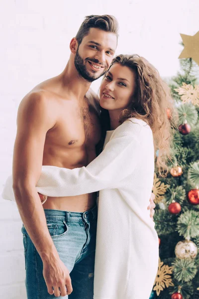 Krullend Lachende Vrouw Knuffelen Shirtless Gespierde Vriendje Buurt Van Kerstboom — Gratis stockfoto