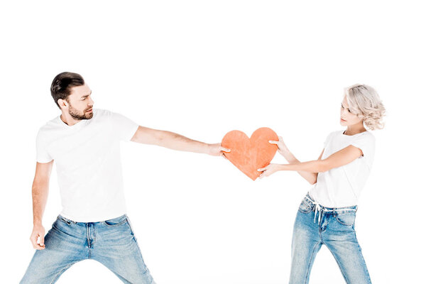 Young adult couple pulling one red big heart shape to each other isolated on white