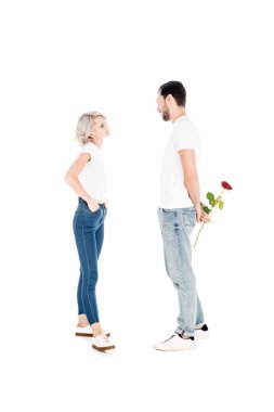 Beautiful couple looking at eahc other while man holding flower behind the back isolated on white  clipart