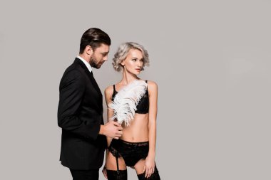 Attractive couple of yound adult woman in lingerie and man with feather isolated on grey  clipart