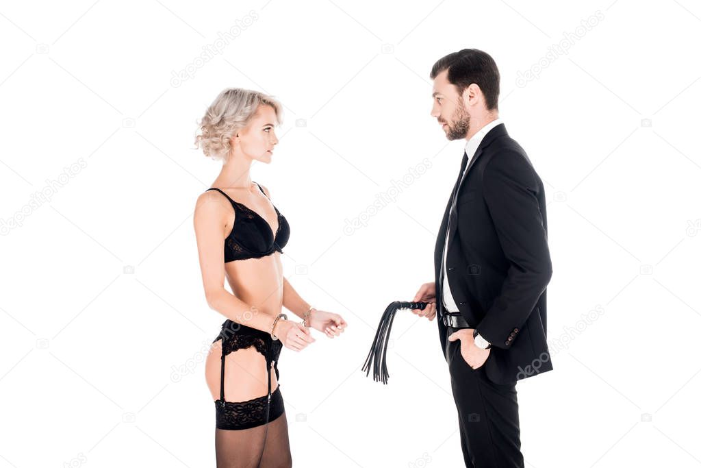 Handsome man holding whip while woman standing in lingerie and handcuffs isolated on white