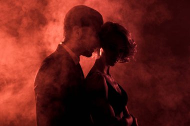 sensual man embracing passionate woman in smoke on red background  clipart