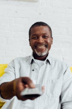 Afro-Amerikan yakışıklı kanepede oturup tv uzaktan kumanda ile gülümseyen