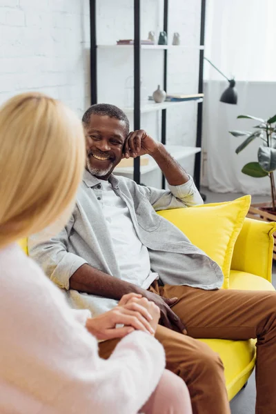 Улыбающийся Взрослый Африканский Американец Сидящий Диване Разговаривающий Блондинкой — Бесплатное стоковое фото