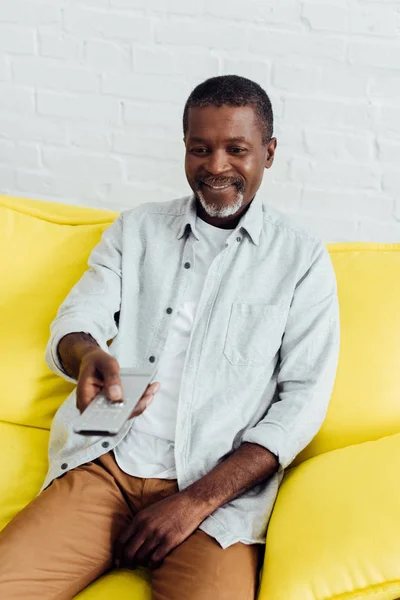 Sorrindo Bonito Afro Americano Homem Sentado Sofá Com Controle Remoto — Fotografia de Stock Grátis