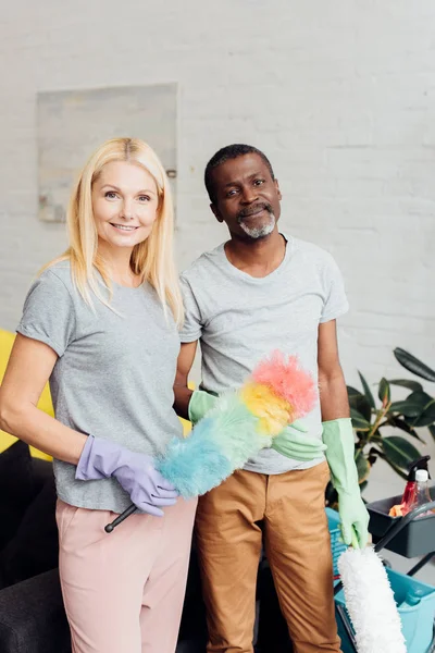 Mujer Rubia Sonriente Hombre Afroamericano Guantes Goma Sosteniendo Plumeros — Foto de Stock