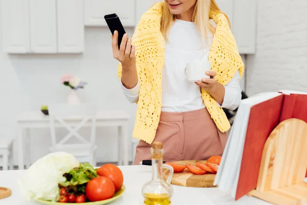 Vista Recortada Mujer Rubia Sosteniendo Teléfono Inteligente Mientras Cocina Cena — Foto de stock gratis