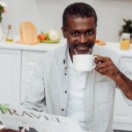 Hombre afroamericano bebiendo café y leyendo el periódico de viajes en la cocina