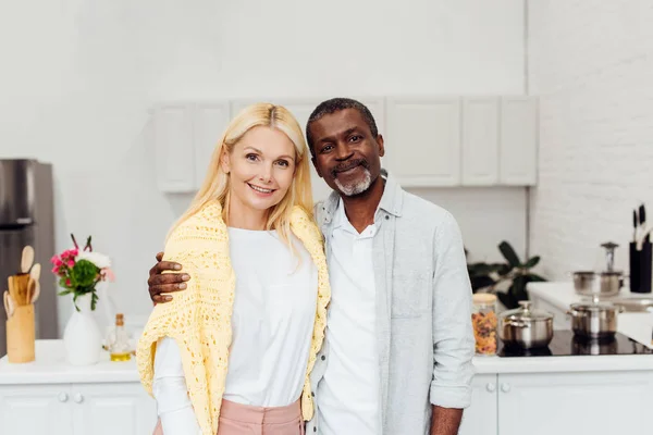 African American Man Hugging Blonde Mature Woman Kitchen — Stock Photo, Image