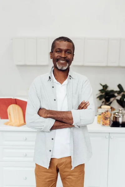 快乐的非洲裔美国人成熟的男人与双臂交叉站在厨房 — 图库照片