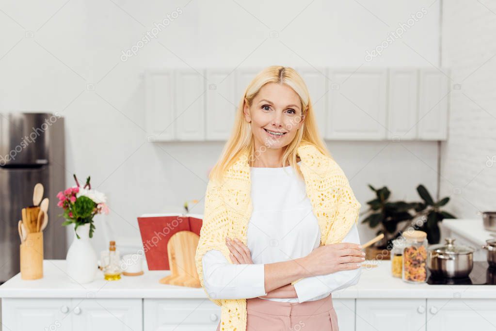 smiling blonde woman with arms crossed standing at kitchen