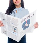 Recortado disparo de sonriente afroamericana mujer leyendo periódico de negocios aislado en blanco