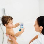 Fils montrant des jouets à la mère brune dans la salle de bain blanche