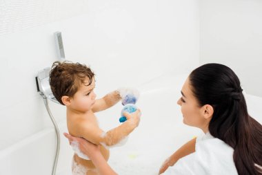 Esmer annesi beyaz banyo için oyuncaklar gösterilen oğlu 