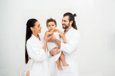 Parents looking at son in white towel and smiling  clipart