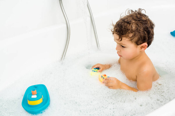 Toddler boy playing with bath toys in white bathroom